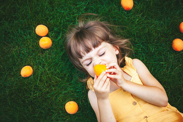 Little girl lying on a grass eating apricot