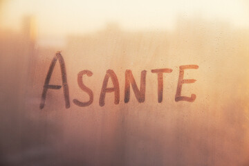 Swahili word Asante thanks in english are painted on wet orange sunrise glass of window