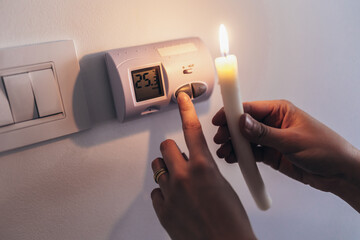 Energy crisis. Man in complete darkness holding a candle to investigate thermostat during a power...