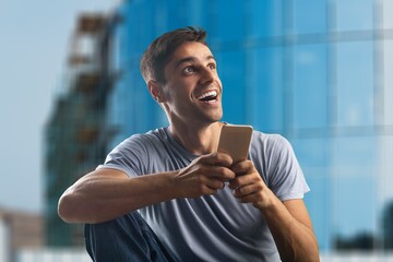 Happy smiling young man looking at smatrphone in his hand with excited face expression,