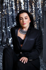 Portrait of a young beautiful woman with dark hair of European appearance. Dressed in a black jacket. Silver shiny background