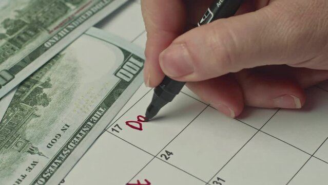 Female hand marking the day in calendar by writing DAY DEBT as a reminder using a red marker.