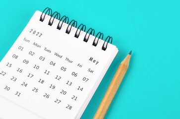 May 2022 desk calendar with wooden pencil on light blue background.