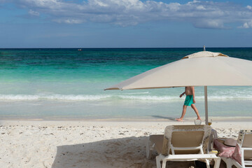 Beach umbrella and partial view of a man walking on the seashore a Caribbean beach in Mexico