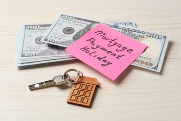 Paper note with words Mortgage Payment Holiday, key and money on white wooden table