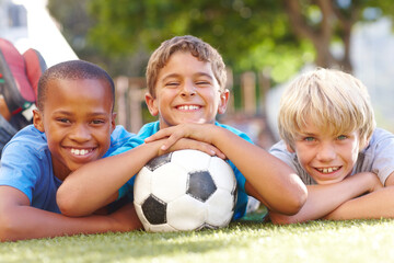 A winning team of best friends. Three happy boys lying outside in the sun with their soccerball - copyspace.