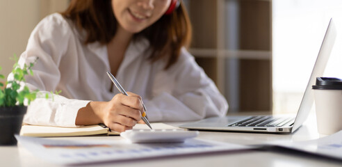 Close-up woman working on desk writing notes on notepad.