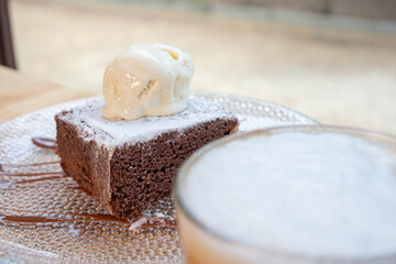 Delicious hot vegan chocolate brownie topped with vanilla ice cream accompanied by a coffee with milk. Vegan breakfast in a bar.