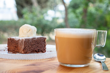 Delicious hot vegan chocolate brownie topped with vanilla ice cream accompanied by a coffee with milk. Vegan breakfast in a bar.