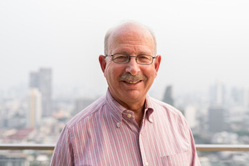 Portrait of smiling senior man looking at camera in city at rooftop - 491647323