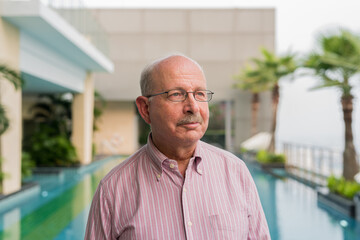 Portrait of senior man smiling and thinking next to swimming pool outdoors