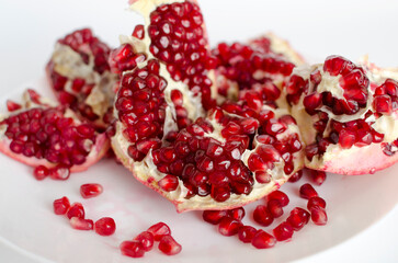 Red pomegranate cut seeds are fresh close-up on a white plate. Juicy fruit, vitamins