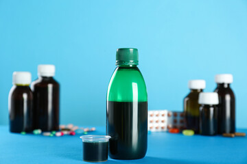 Bottle of cough syrup and measuring cup on light blue background
