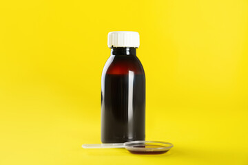 Bottle of cough syrup and dosing spoon on yellow background