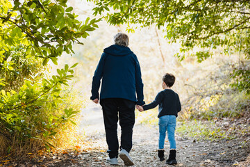 Unrecognizable grandfather and grandson walking in forest during autumn