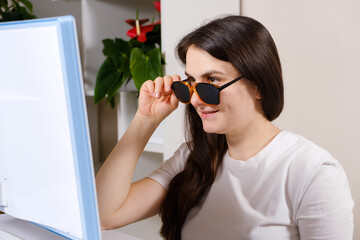 A woman looks at a computer screen through perforated glasses with holes to improve vision in...