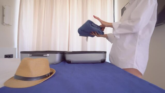 a young beautiful woman in a white shirt takes things out of a suitcase upon arrival on vacation or after vacation. . With a smile on her face, she is going to rest. Apartment or hotel room.