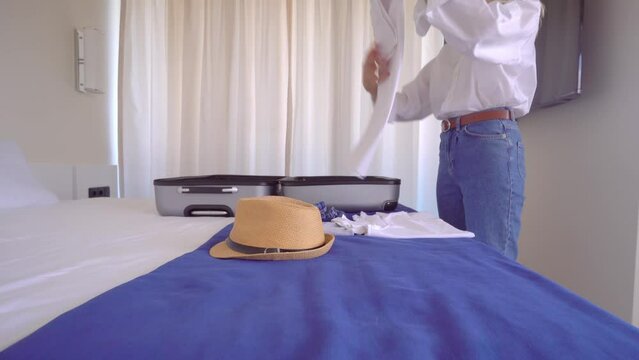 A young beautiful woman in a white shirt and jeans is packing things in a suitcase after a vacation or before a vacation. With a smile on her face, she is going to rest. Apartment or hotel room.