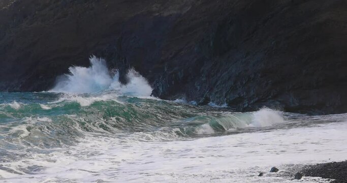 Atlantic blue wave exploding dramatically through blowhole against a black cliff with great contrast in slow motion