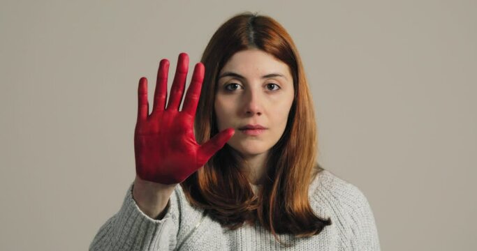 Sad girl raises her hand painted red to stop and protest against violence