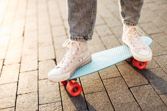 Women's legs in jeans and sneakers ride a skateboard