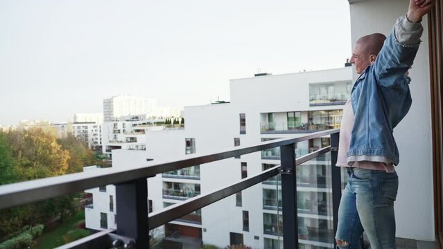 young millenial bold man morning strech on balcony - medium long shot. High quality 4k footage