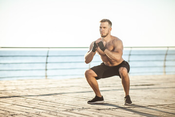 Athletic man practicing squats in the early morning on the beach