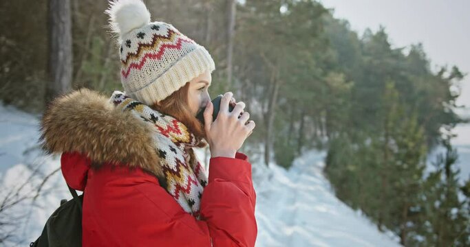 Woman backpacker traveler camper drinking hot tea and relaxing in winter forest, beautiful snow landscape on sunny day. Health care, authenticity, sense of balance. 4 K video