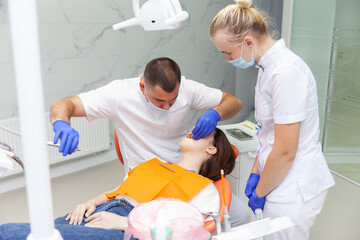 Obraz premium Dentist with assistant examines the oral cavity of female patient in dental clinic. Visit to the dentist. Dental treatment