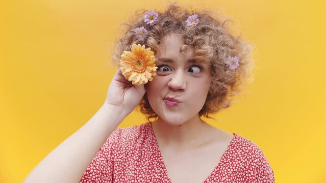 Sweet curly hair girl is playing with a sunflower on her hair. Portrait isolated in yellow