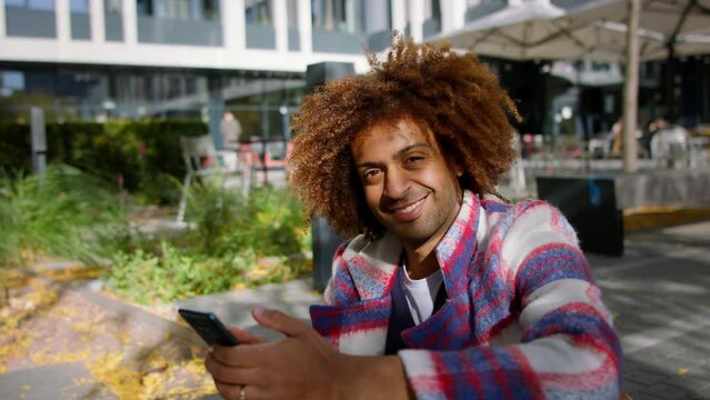 Cool multiracial mid audlt man with smartphone outdoors in town