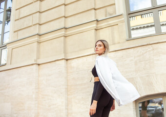 Young fashion blonde woman in white trendy jacket posing in city. Street fashion