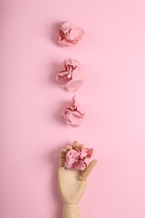 Hand holds crumpled sheets of paper on a pink background. Minimal flat lay still life