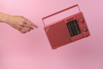 Hand reaches for levitating retro fm radio receiver on pink background