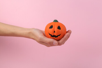 Hand holds antistress toy in the form of pumpkin jack lantern head on pink background. Halloween concept