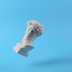 Levitating Antique Plaster bust of David on blue background. Conceptual pop. Minimal still life photography