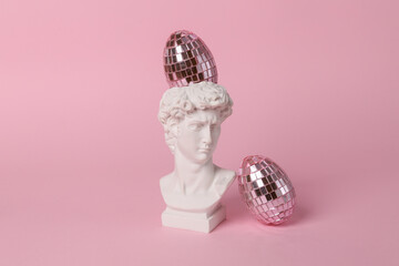 Antique bust of David with mirror eggs on a pink background. Conceptual pop. Minimal easter still...