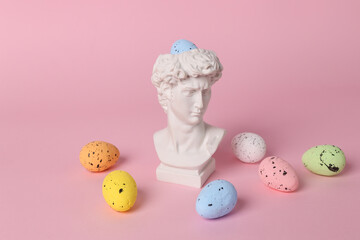 Antique bust of David with colored eggs on a pink background. Conceptual pop. Minimal easter still life. Creative idea