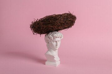 Antique bust of David with nest on a pink background. Conceptual pop. Minimal still life. Creative idea