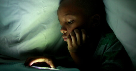 Young boy looking at cellphone screen at night under blanket