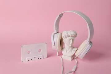 Antique bust of David with headphones and audio cassette on pink background. Conceptual pop....