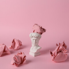 Antique David bust with crumpled paper balls on pink background. Conceptual pop. Minimal still life. Creative idea