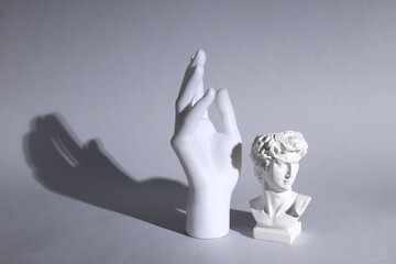 David's bust with hand monument on gray background with long shadow. Minimal still life