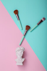 David bust with makeup brushes on pink blue background. Creative layout. Minimal beauty still life. Flat lay. Top view