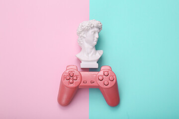 Retro gamepad with David bust on pink blue background. Gaming. Creative layout. Minimal still life. Flat lay. Top view © splitov27