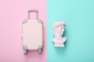Toy baggage with David bust on pink blue background. Creative layout. Minimal travel still life. Flat lay. Top view