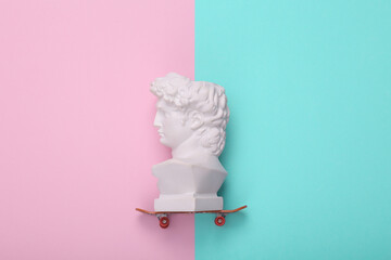 David bust ride on skateboard, pink blue background. Creative layout. Minimal still life. Flat lay. Top view