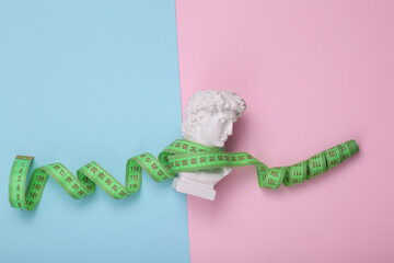 David bust wrapped with measuring tape on pink blue background. Creative layout. Diet Concept....