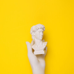 Hand holding David bust on yellow background. Minimal still life