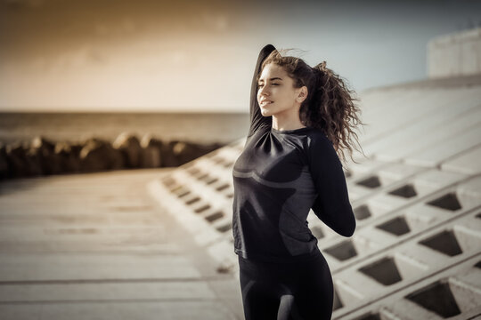 Outdoor workout concept. Fit slim woman with curly hair stretches or warms up on an urban embankment with concrete slabs
